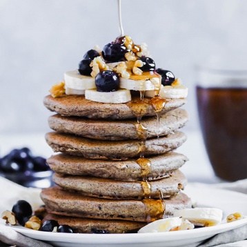 a stack of buckwheat pancakes topped with fruit, buts and maple syrup