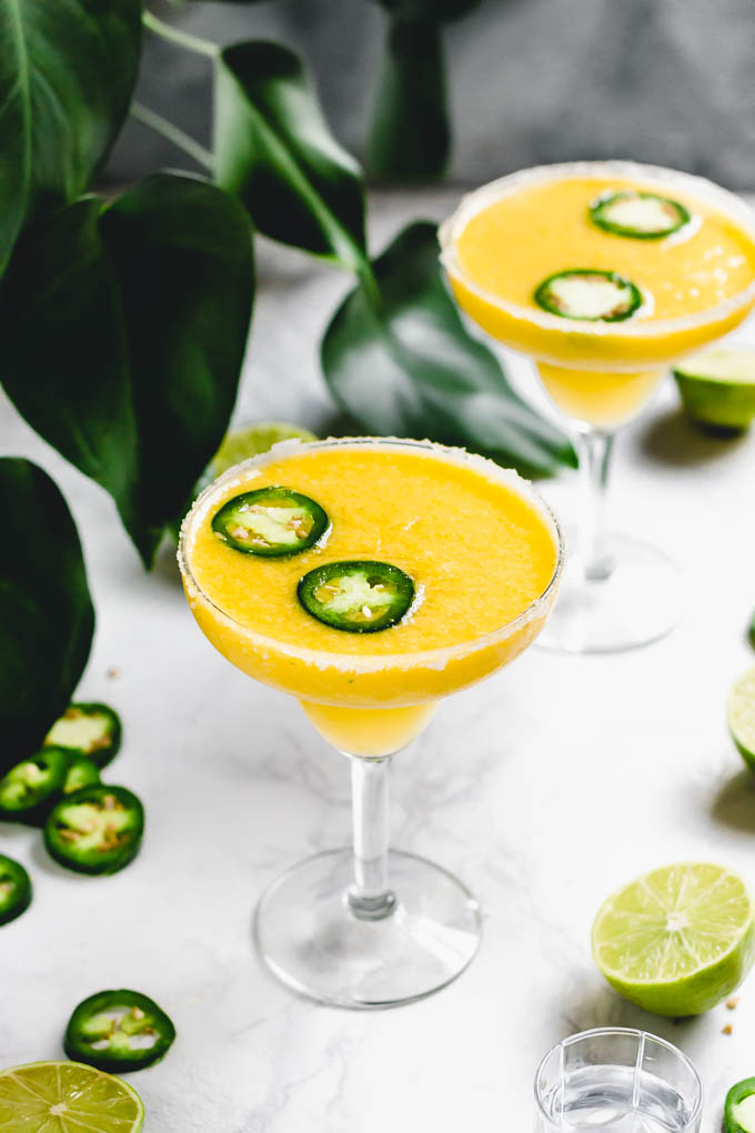 two glasses filled with mango margaritas topped with slices of jalapeno