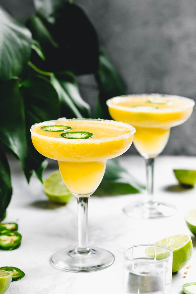 two mango margaritas topped with jalapeno slices