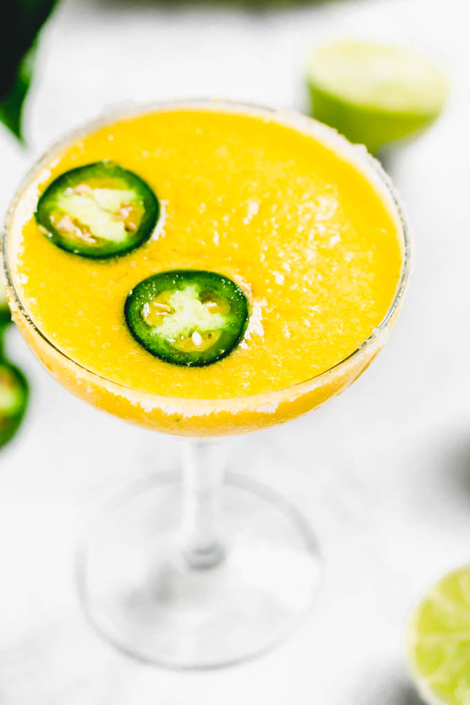 a close up shot of a frozen mango margarita topped with jalapeno slices