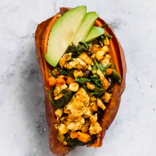 A baked sweet potato filled with tofu scramble and topped with sliced avocado