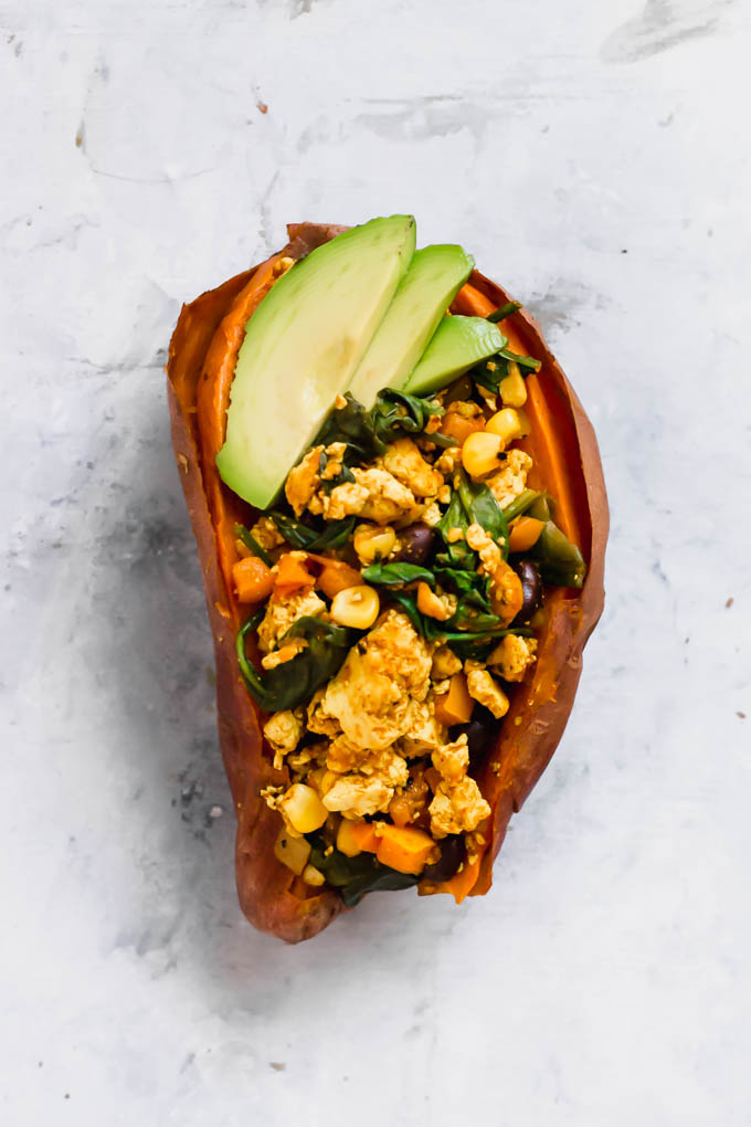 A baked sweet potato filled with tofu scramble and topped with sliced avocado