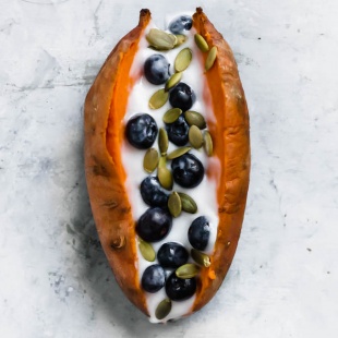 a baked sweet potato topped with vegan yogurt, blueberries and pumpkin seeds