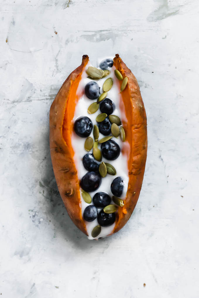 a baked sweet potato topped with vegan yogurt, blueberries and pumpkin seeds