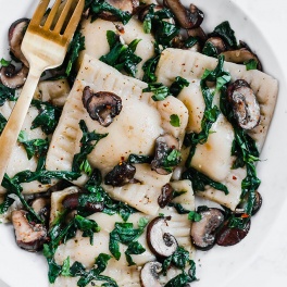 a bowl of ravioli with greens and mushrooms