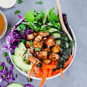 a vegan poke bowl featuring tofu, seaweed, greens, cucumber, carrots and cabbage