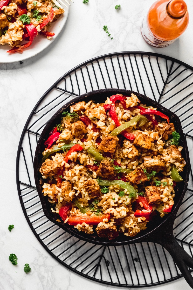 A cajun rice and tempeh dish served in a cast iron skillet alongside a bottle of hot sauce