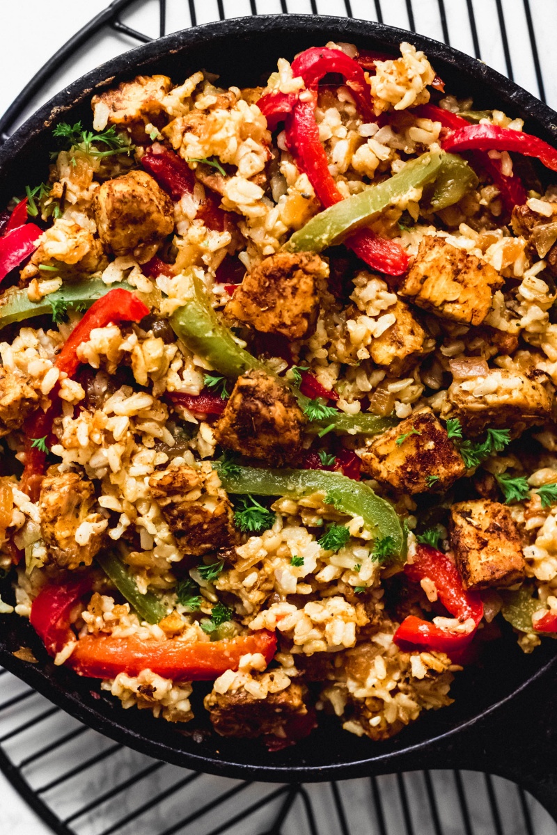 A close up shot of a vegan tempeh and rice skillet served with green and red bell peppers and topped with fresh parsley