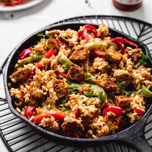 A cast iron skillet serving vegan cajun rice and fried tempeh with red and green bell peppers