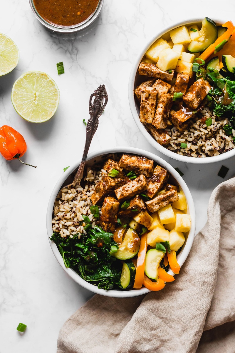 two jerk tofu power bowls next to two halves of a lime