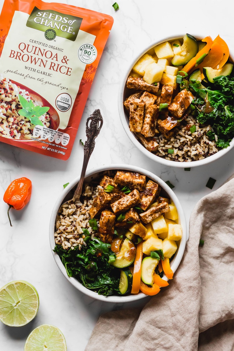 two bowls filled with brown rice, tofu, veggies and pineapple