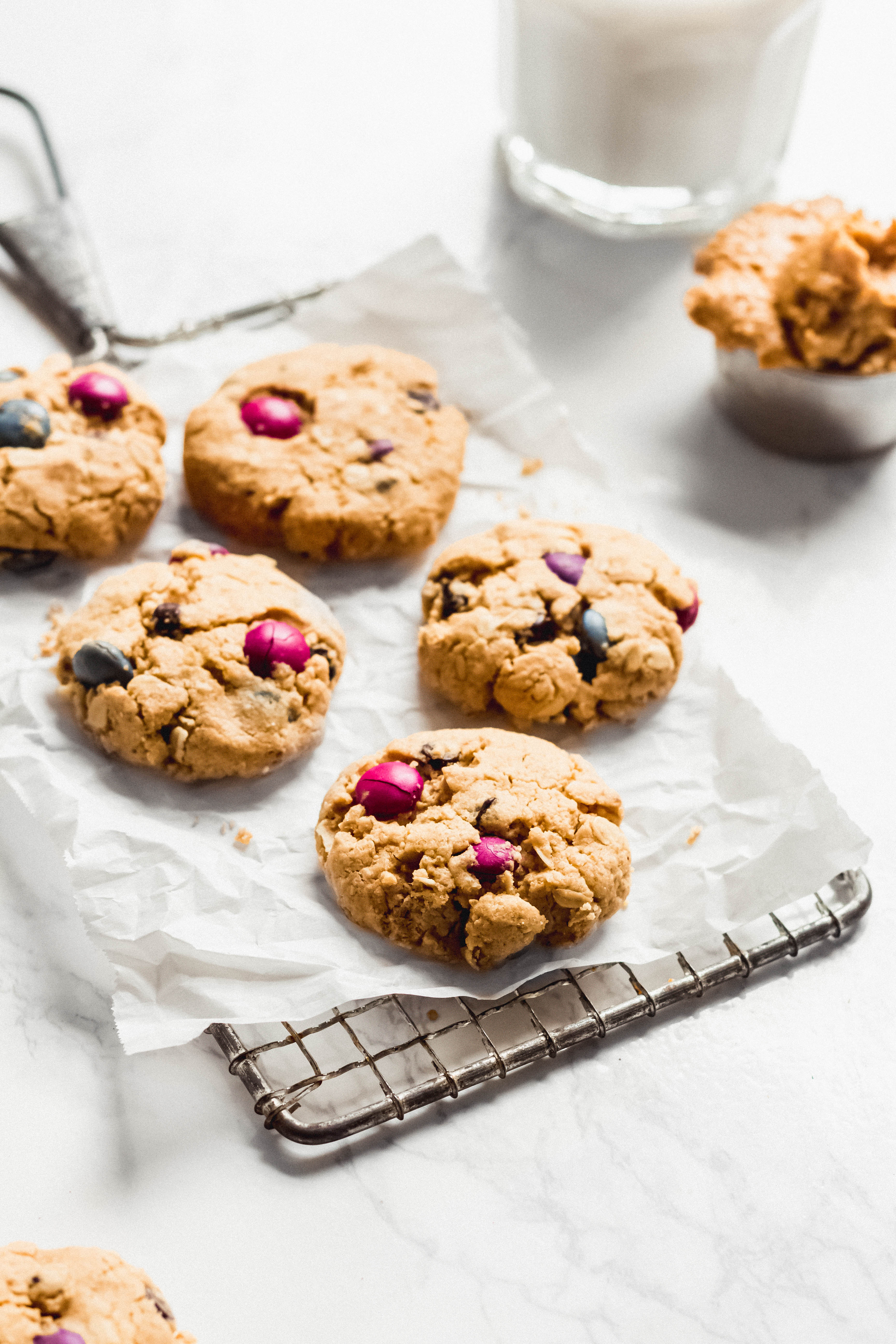 a closeup of a batch of vegan monster cookies cooling on a wire rack