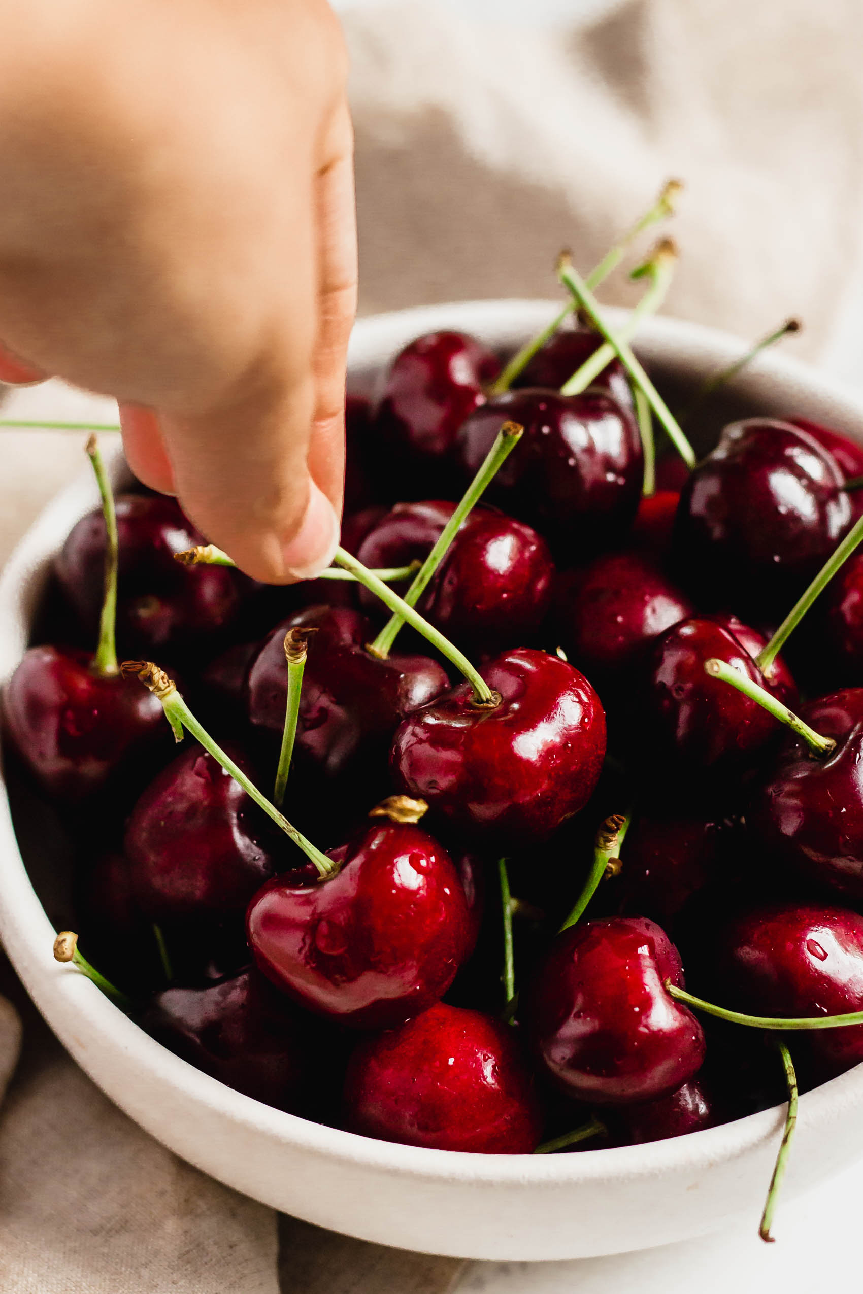 a hand reaching for a cherry out of a bowl