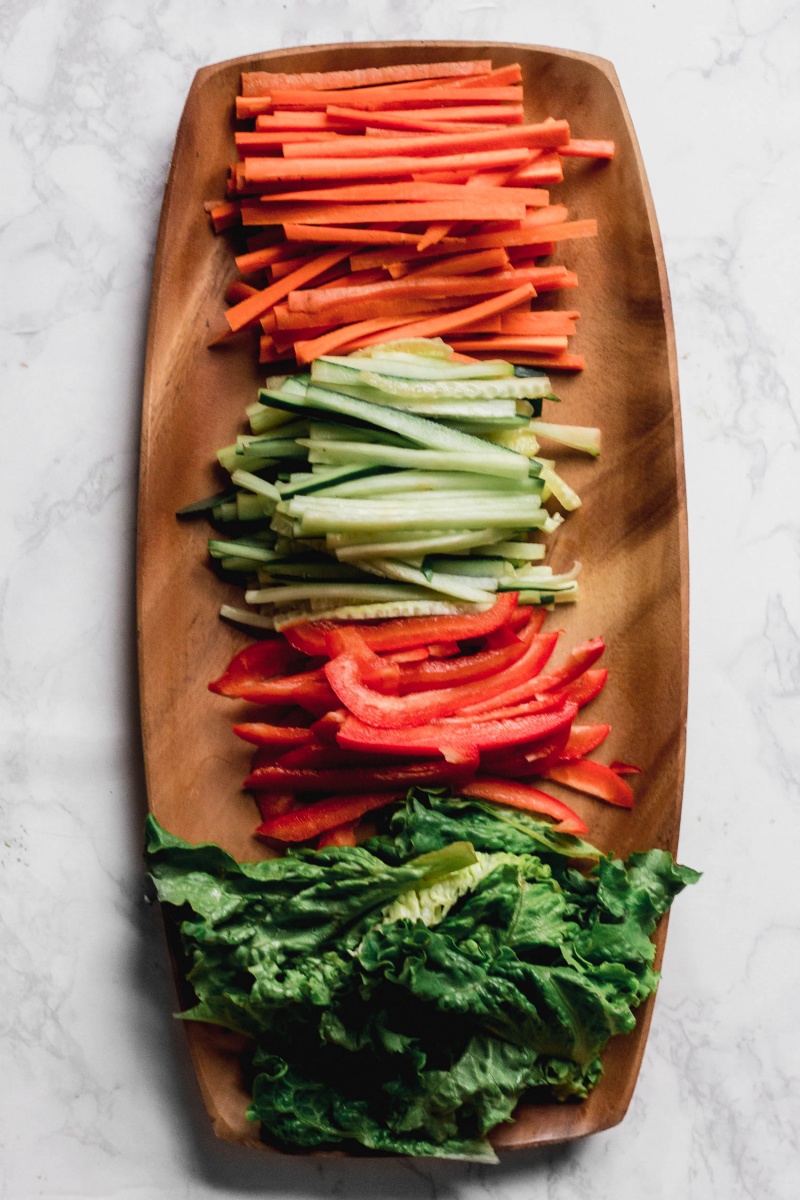 a wooden platter holding sliced carrots, cucumber, red bell pepper and lettuce