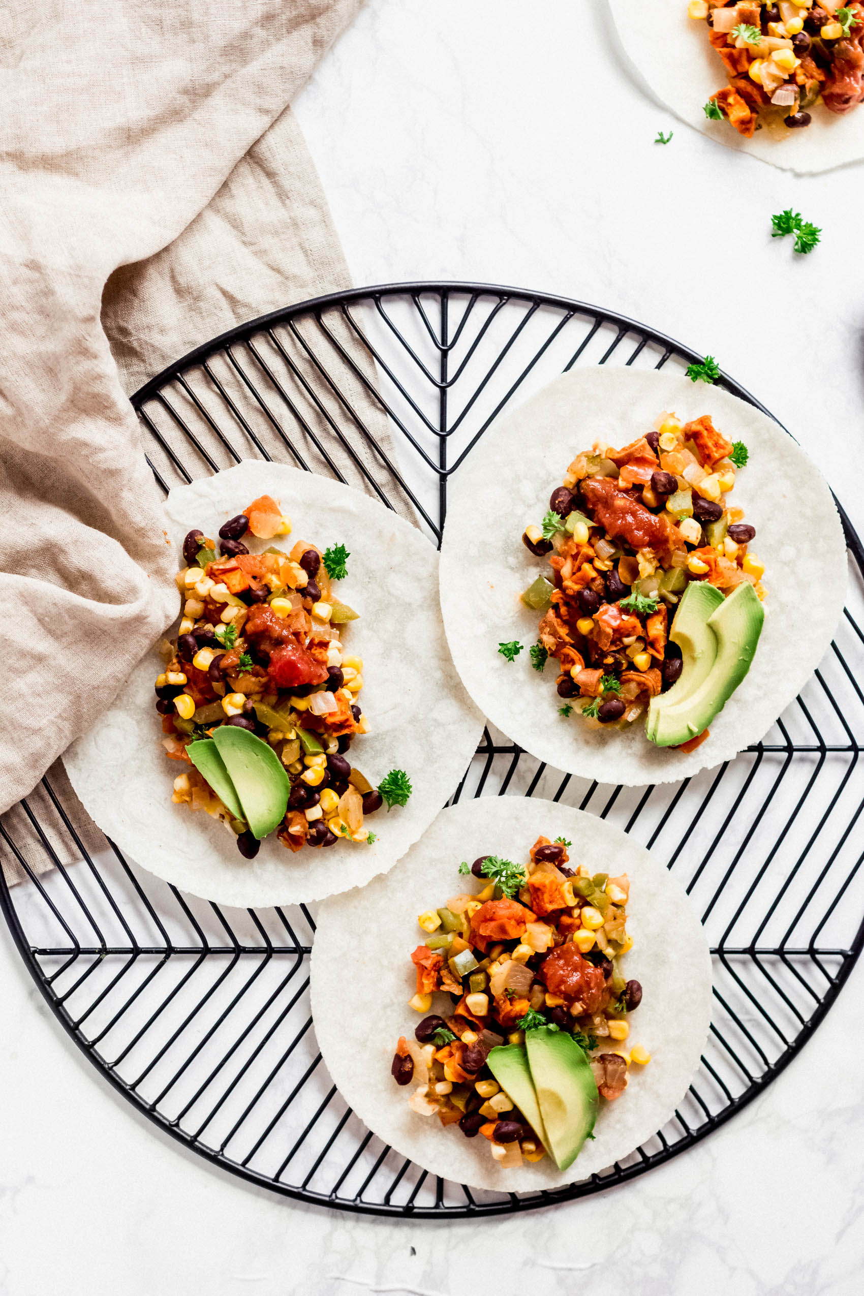 three sweet potato and black bean tacos topped with sliced avocado