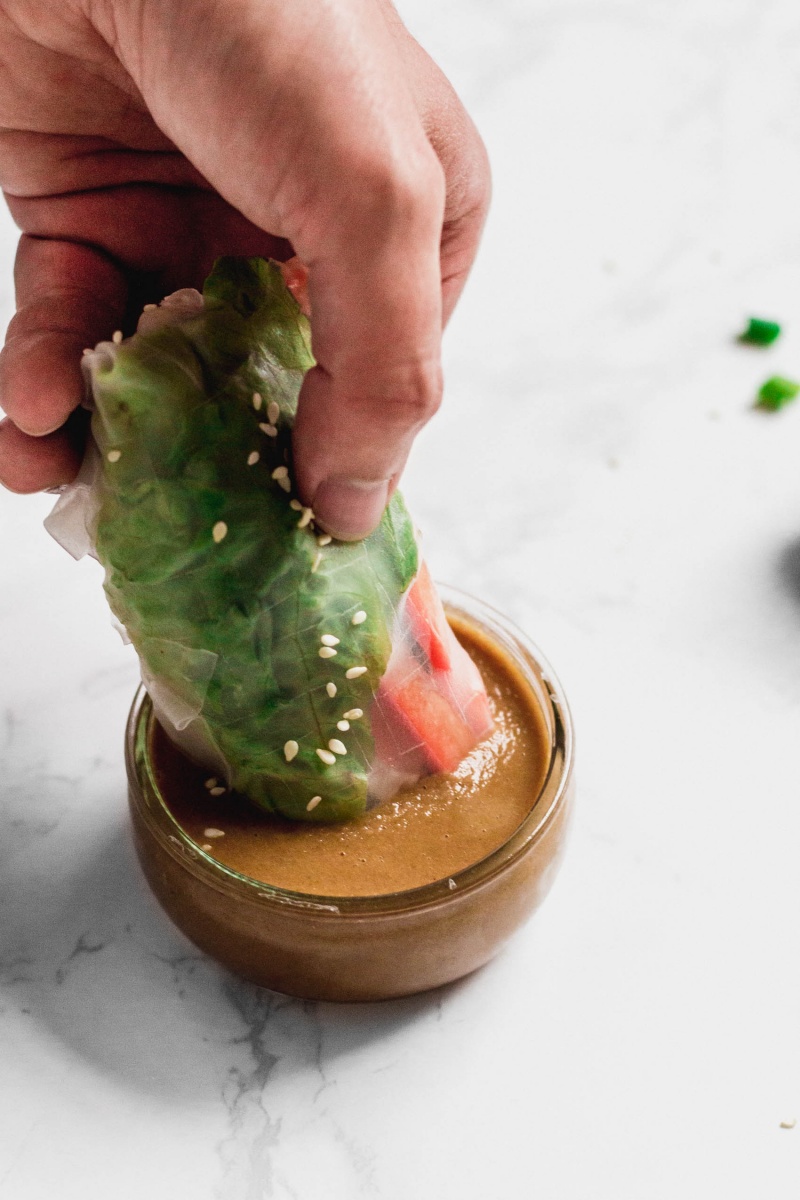 A spring roll being dipped into a tahini sesame ginger sauce