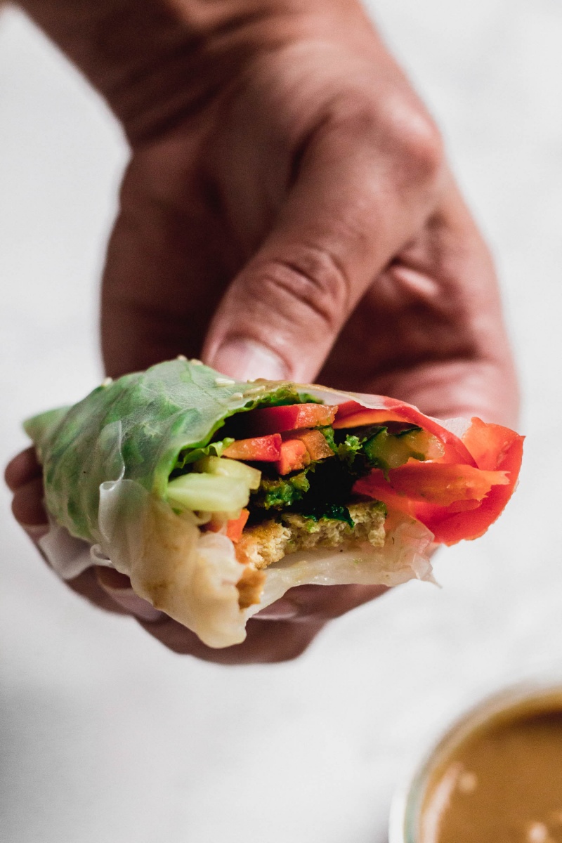 A hand holding a spring roll with a bite taken out of it