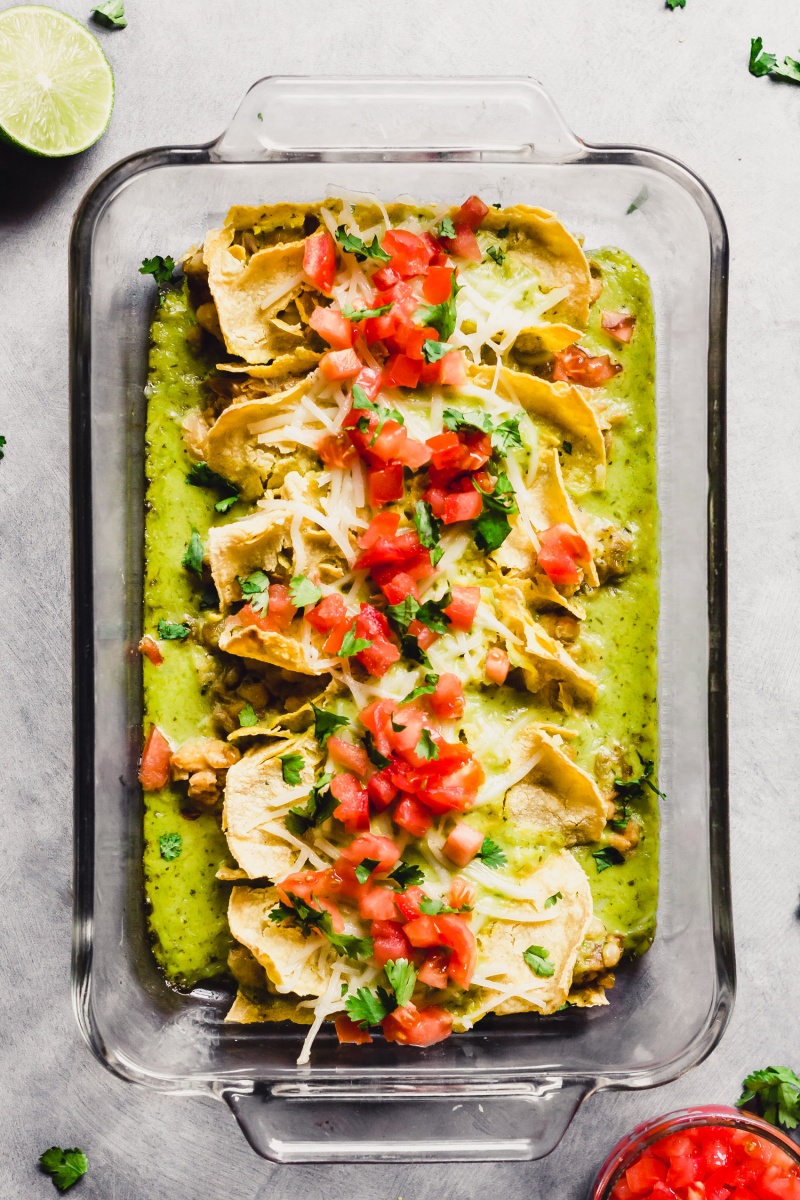 A pan of green chili enchiladas topped with diced tomatoes and cilantro