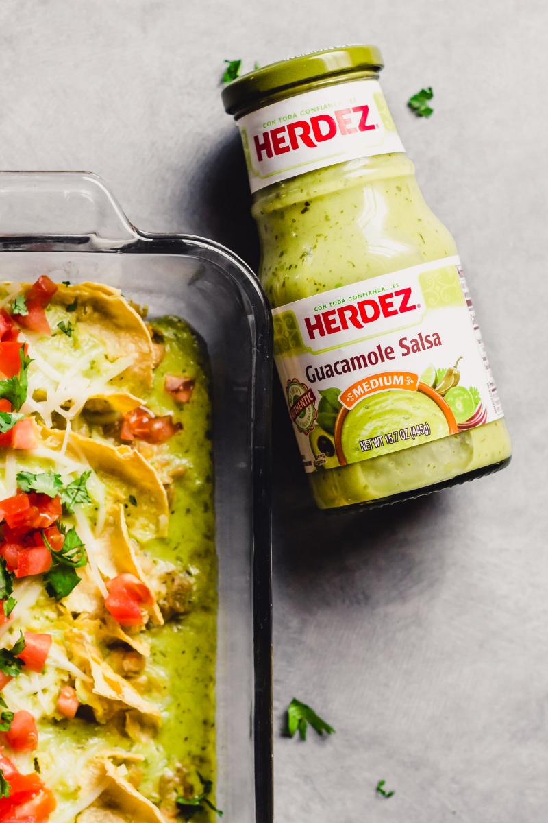 A jar of Herdez guacamole salsa next to a dish of green chili enchiladas