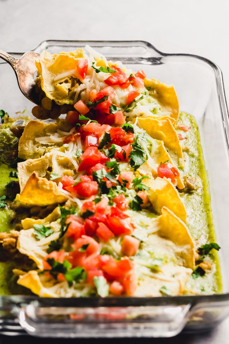 A spatula scoops out a serving of green chili enchiladas