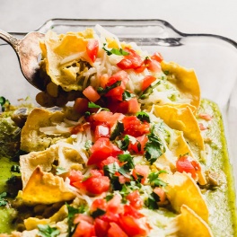 a spatula digs into a dish of vegan enchiladas