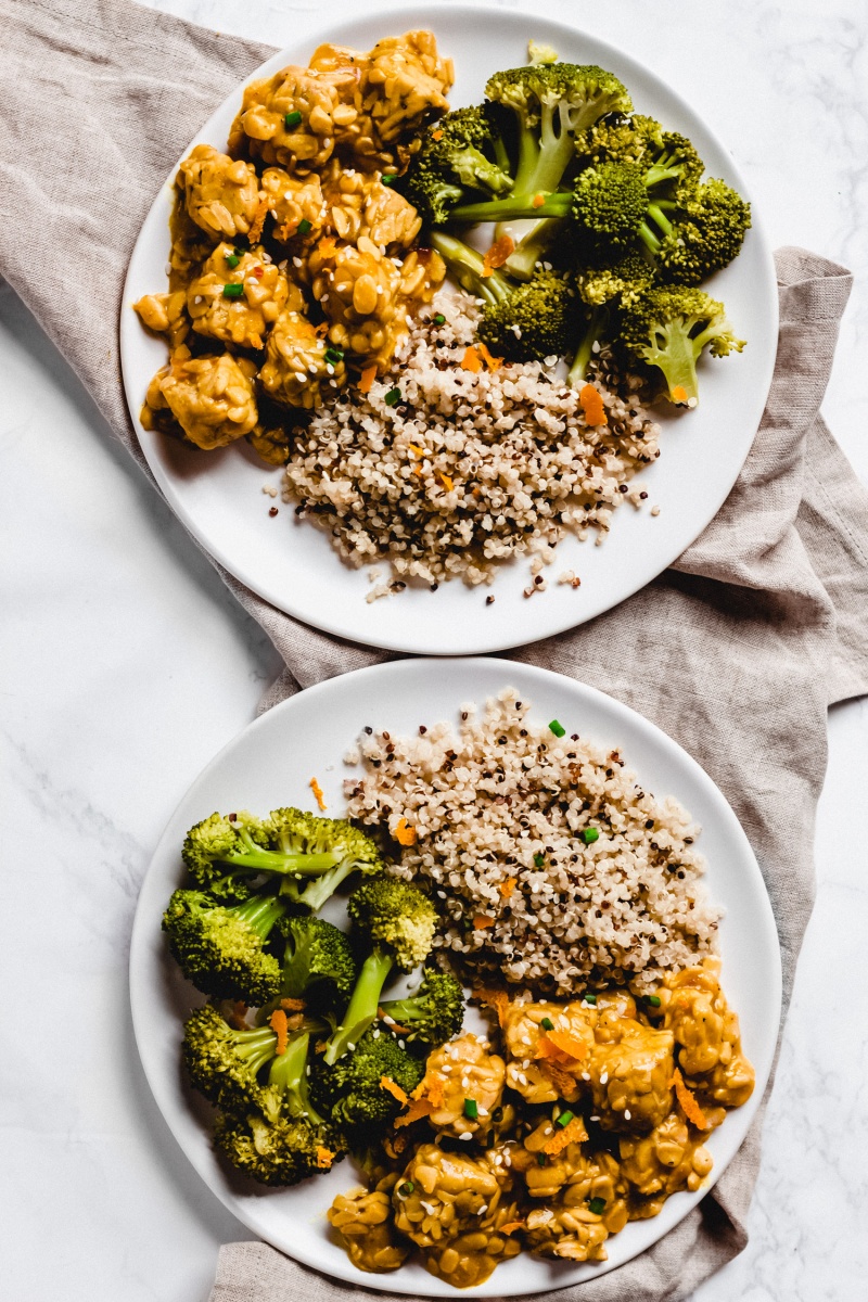 Two plates of vegan orange tempeh served with broccoli and quinoa