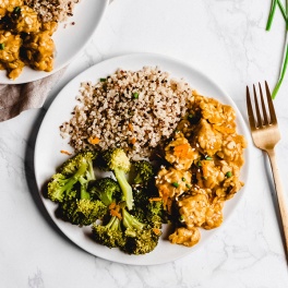 A plate of tempeh covered in orange stir fry sauce and served alongside broccoli and quinoa