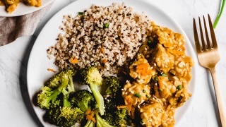 A plate of tempeh covered in orange stir fry sauce and served alongside broccoli and quinoa