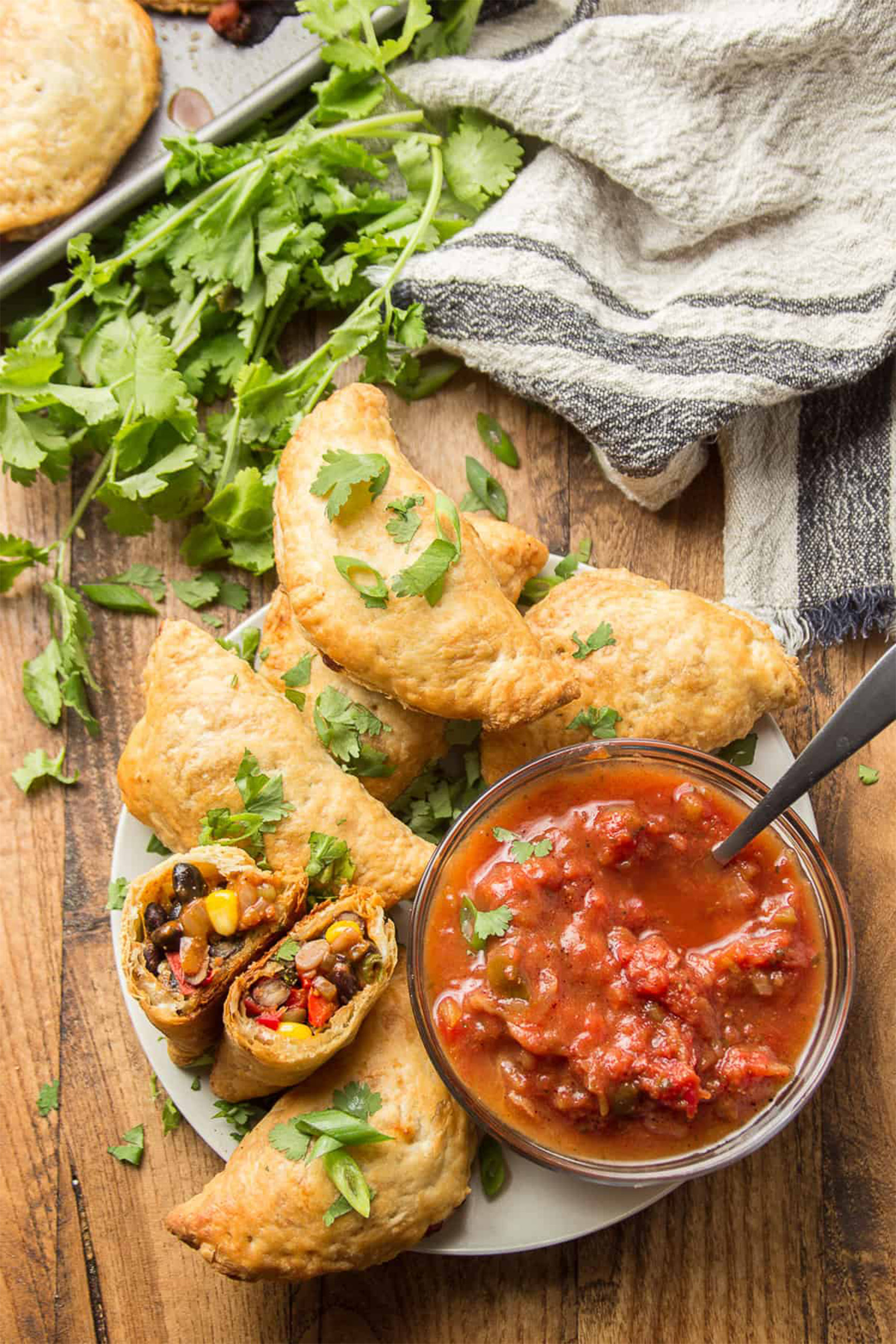 a plate of vegan empanadas served with cilantro and salsa