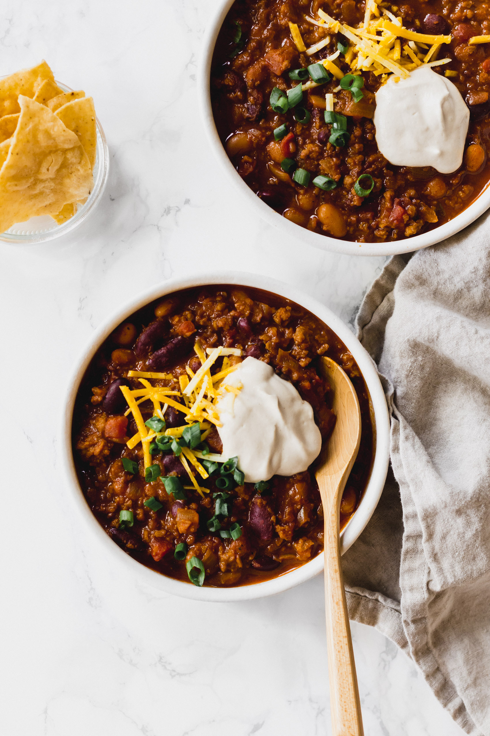 two bowls of vegan chili each topped with scallions, vegan cheese and vegan sour cream
