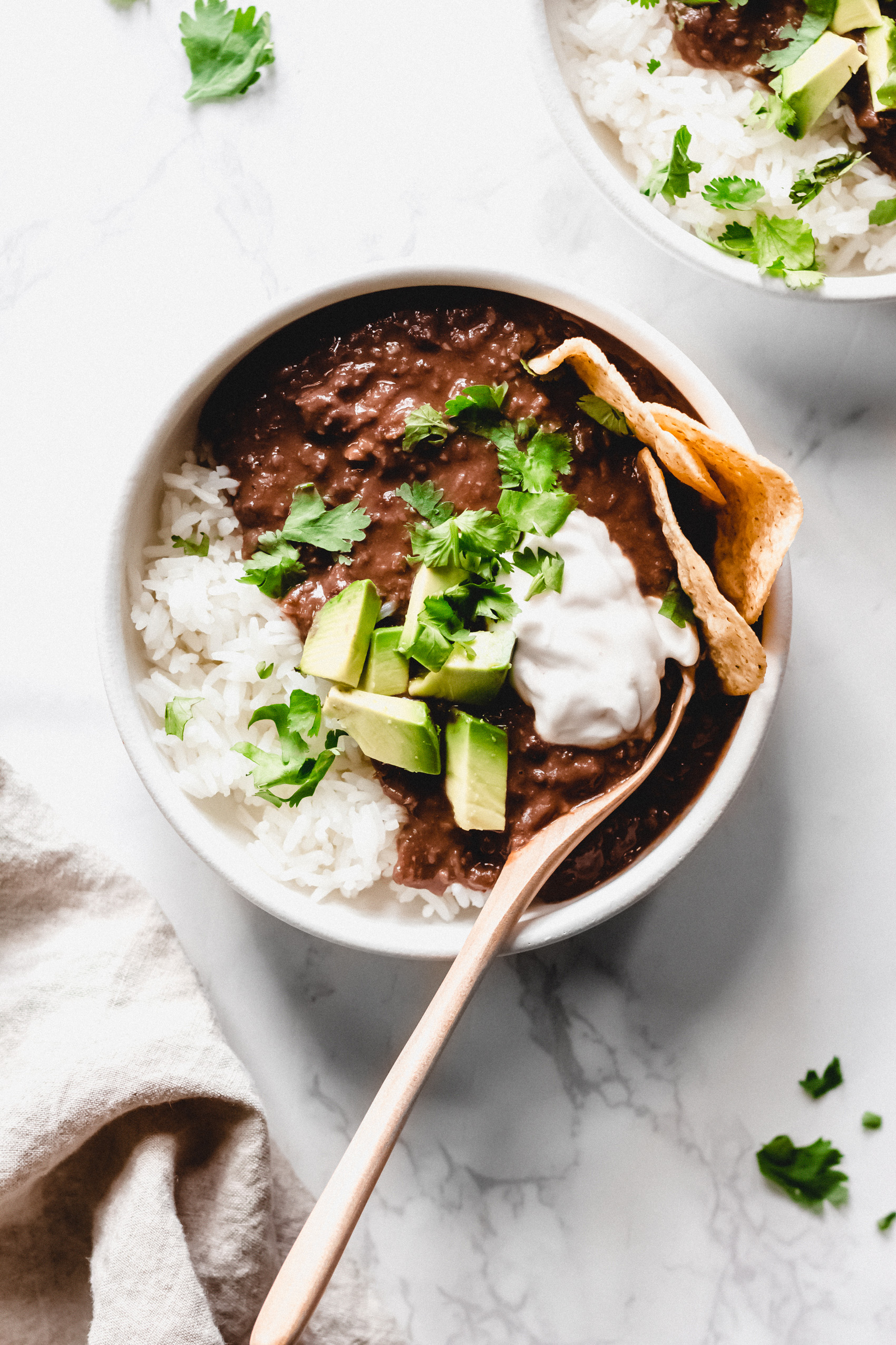 a bowl of black bean soup topped with vegan sour cream, cilantro, avocado and tortilla chips