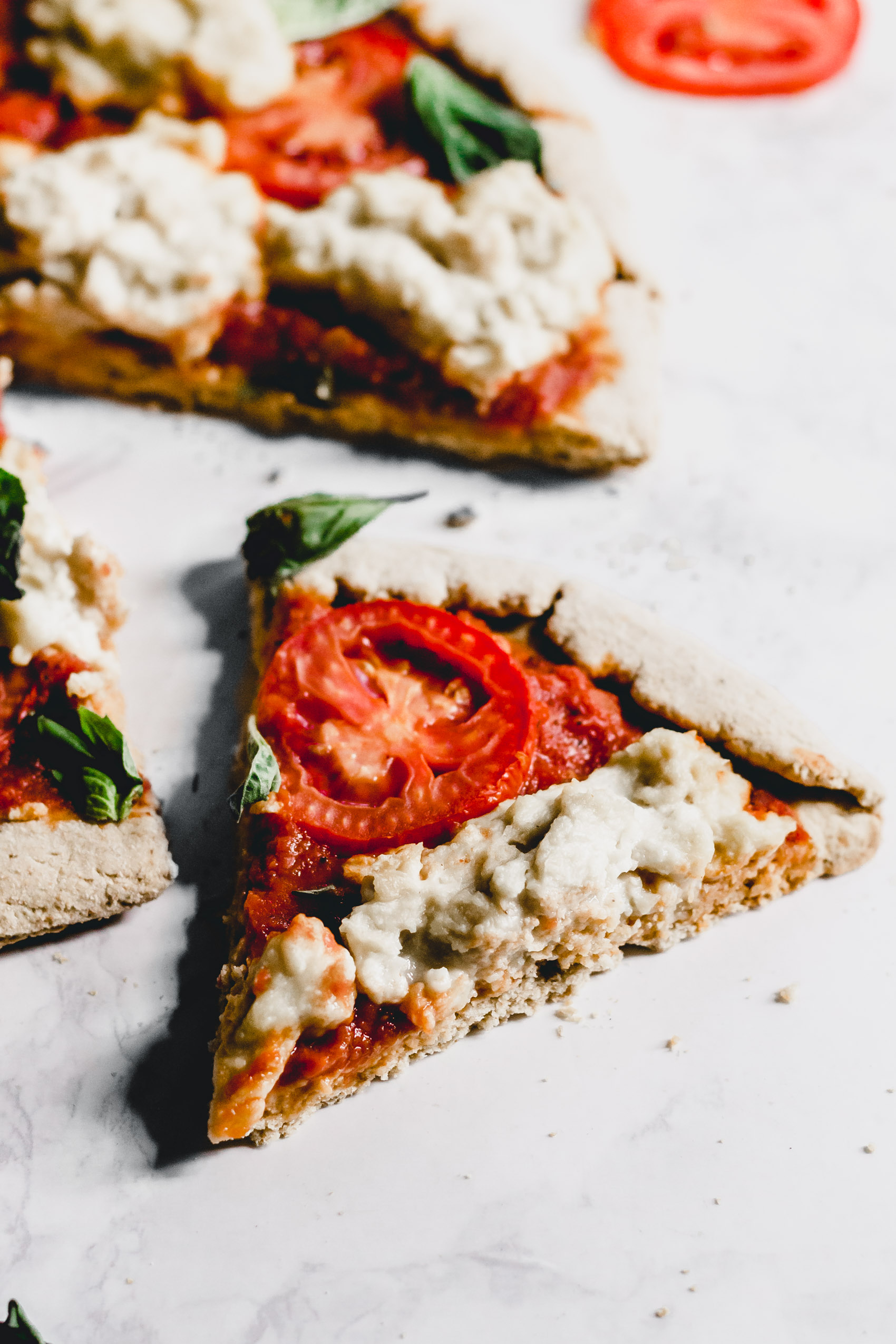 a slice of vegan pizza topped with cashew cheese, tomatoes and basil