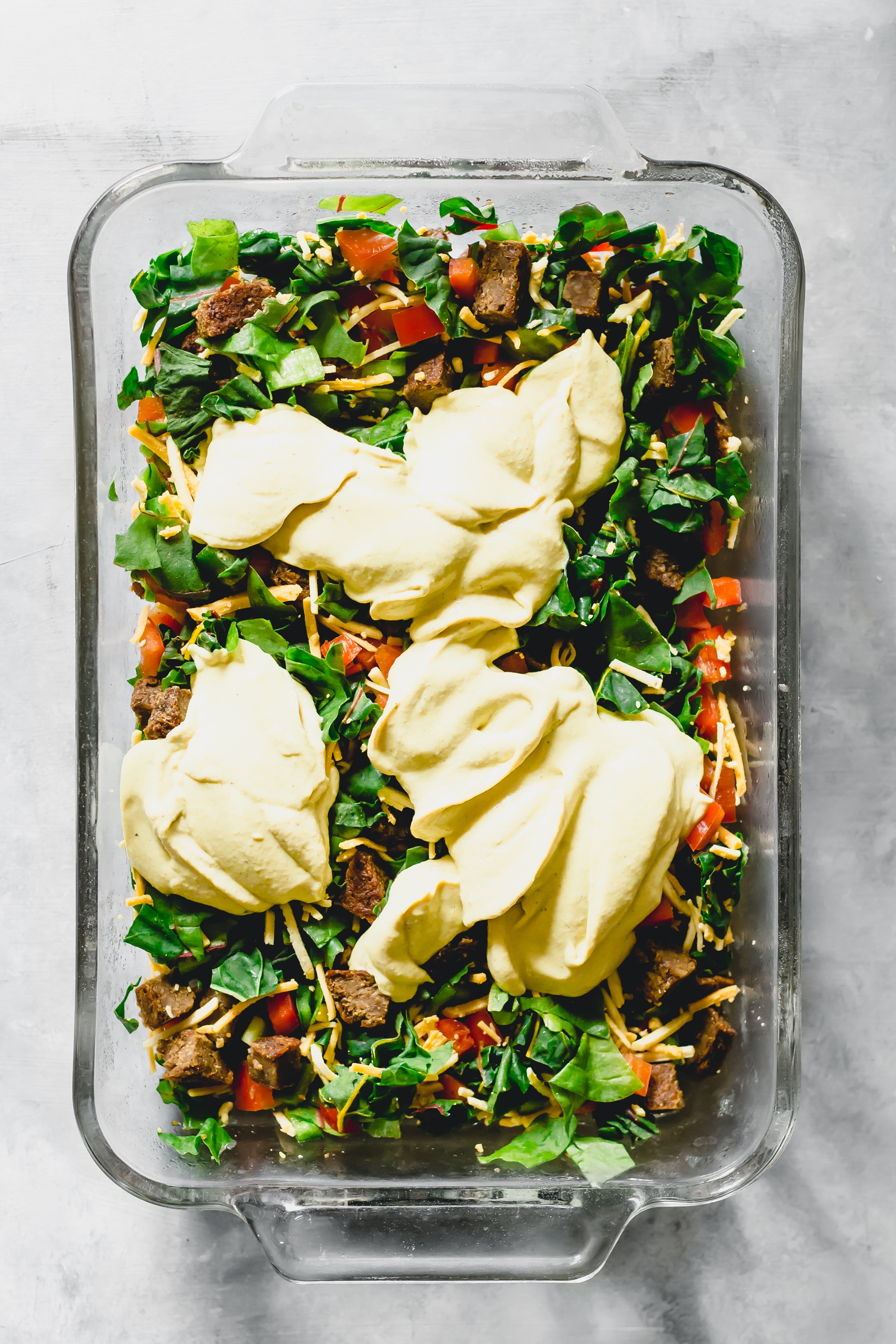 a casserole dish filled with vegetables, greens, vegan cheese and a vegan egg mixture
