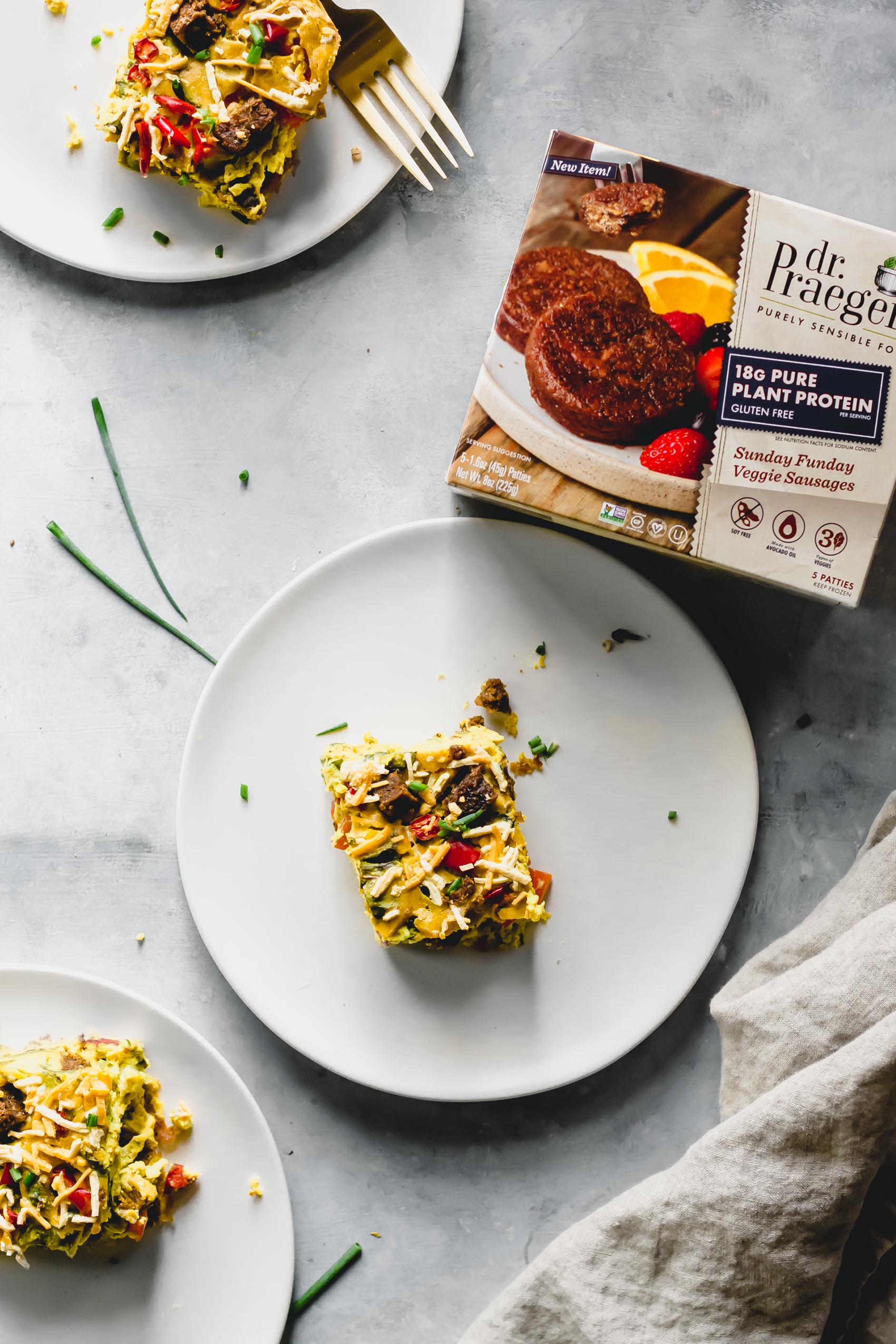 a slice of vegan egg casserole on a plate next to a box of vegan sausages