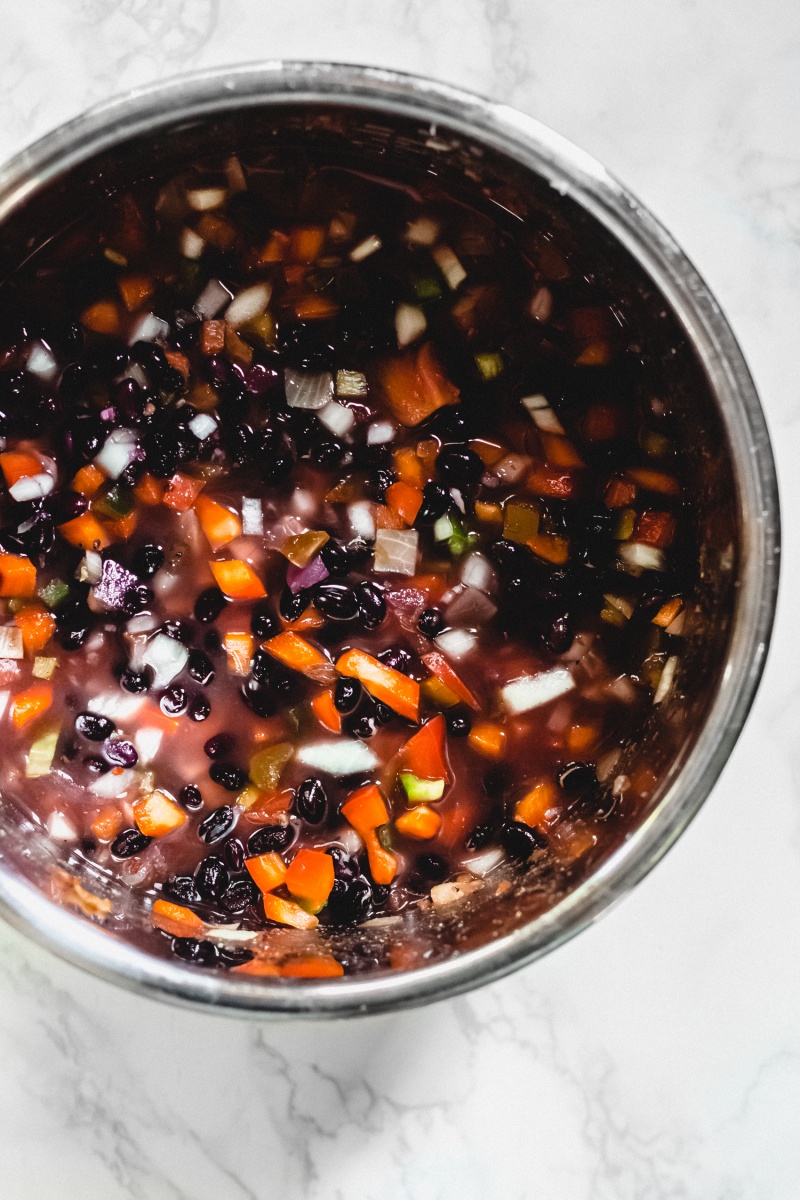 a slow cooker filled with black beans, chopped veggies and broth