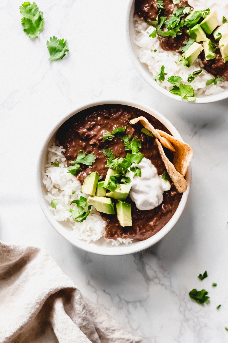 a bowl of black bean soup topped with cilantro, sour cream, chips and avocado chunks