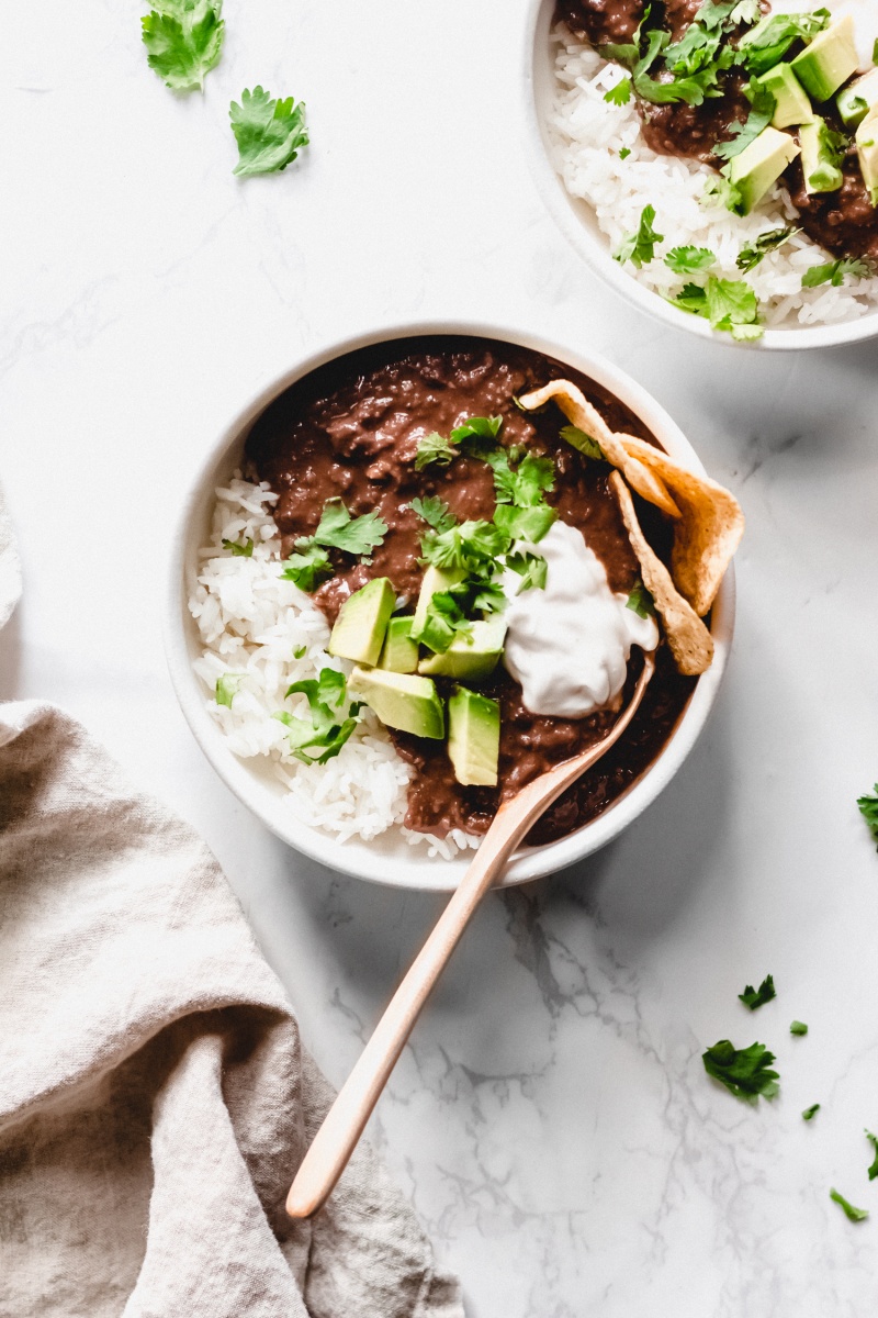 a bowl of black bean soup served with rice, chips, avocado and vegan sour cream