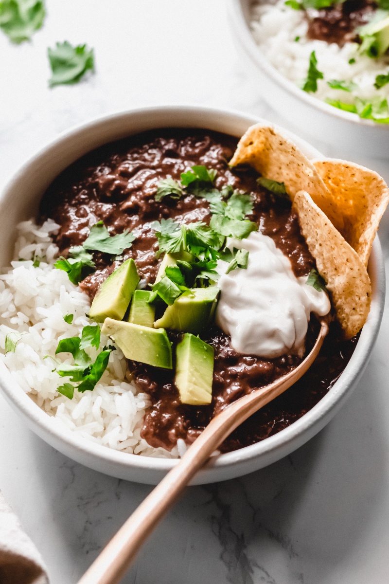 a bowl of black bean soup topped with vegan sour cream, avocado, cilantro and tortilla chips