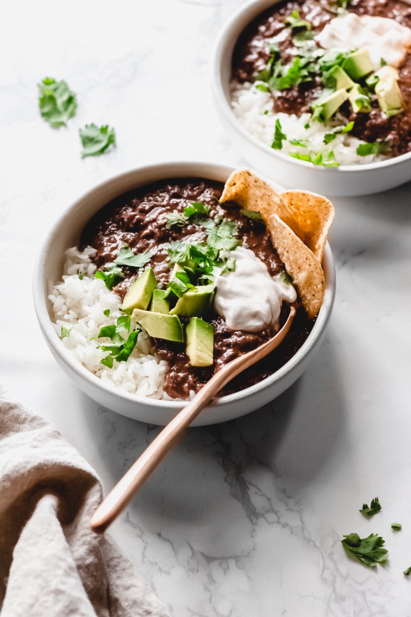 a bowl of black bean soup served with rice, avocado, dairy free sour cream and tortilla chips