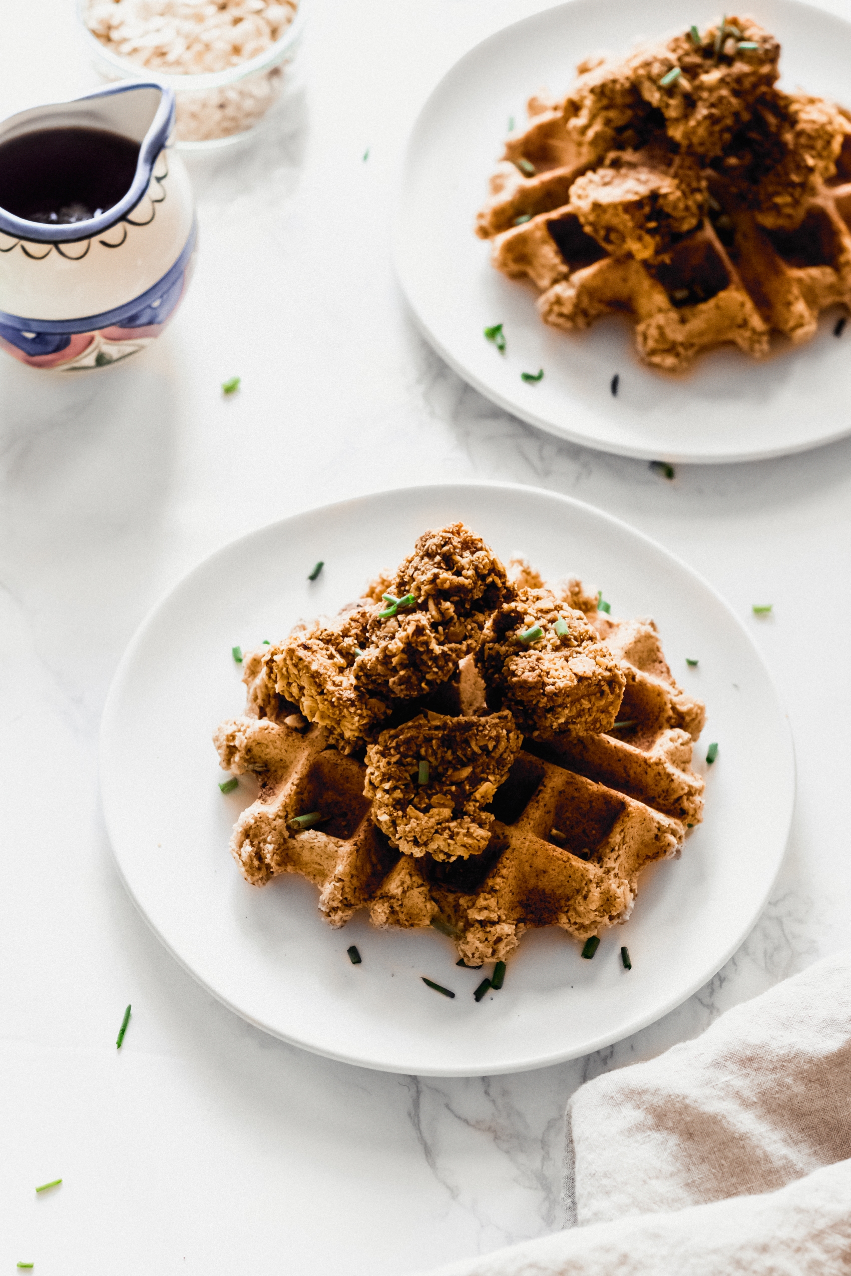 two plates of waffles, each topped with vegan fried chicken
