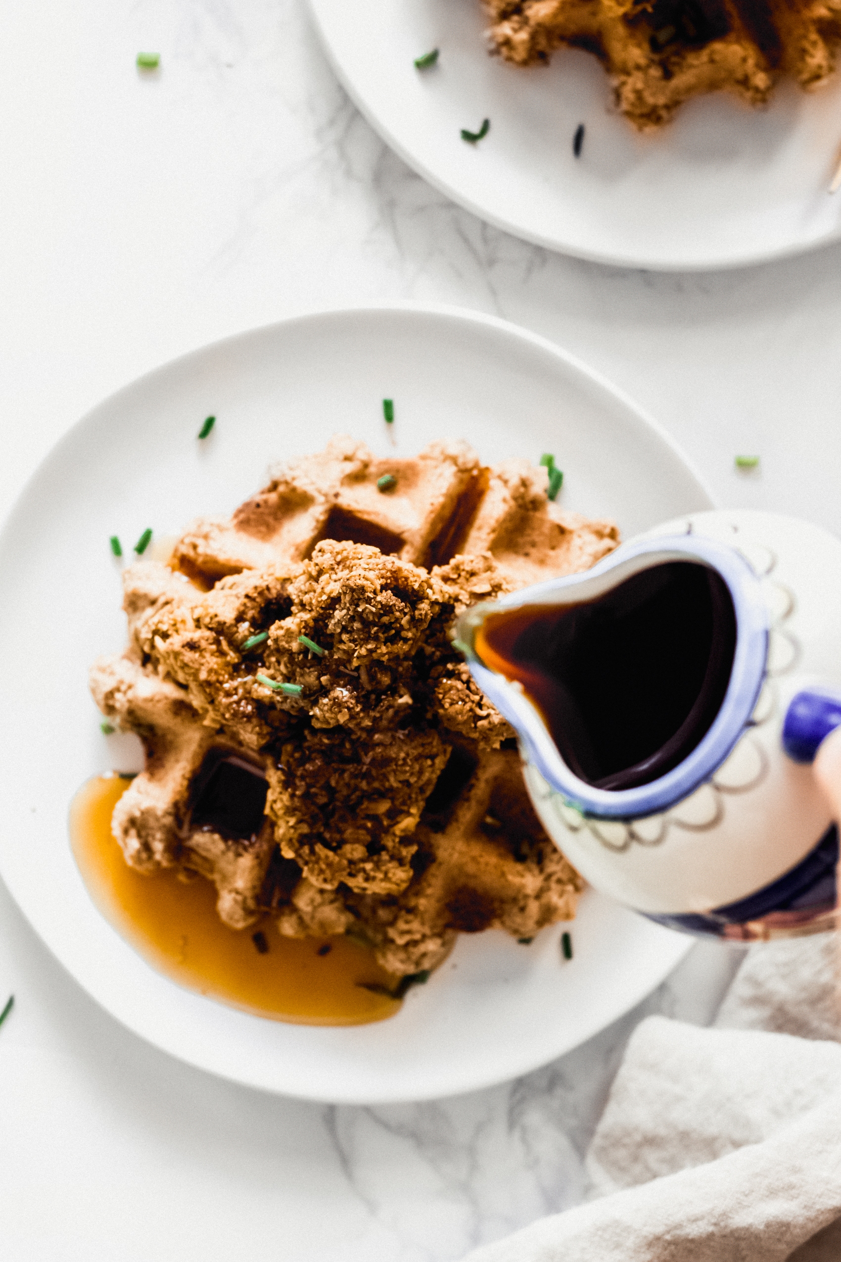 maple syrup being poured onto a stack of vegan chicken and waffles