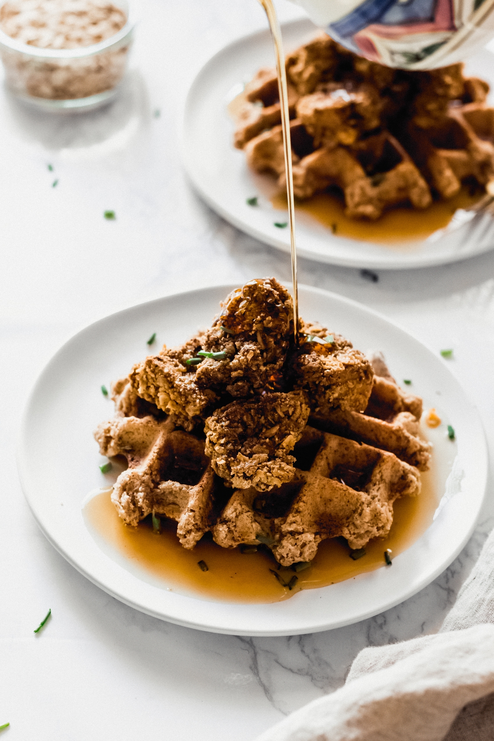 maple syrup being poured on top of a plate of vegan chicken and waffles