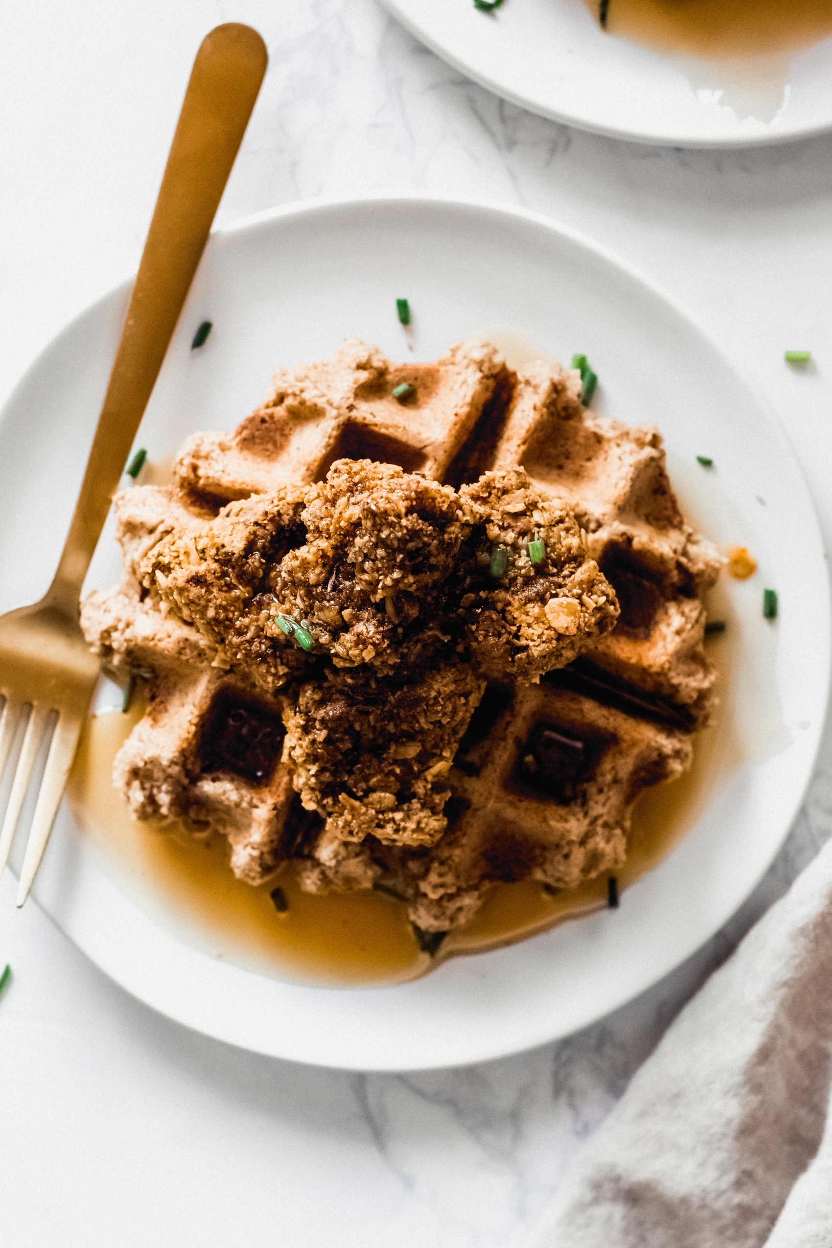 a vegan waffle topped with vegan fried chicken, maple syrup and chives