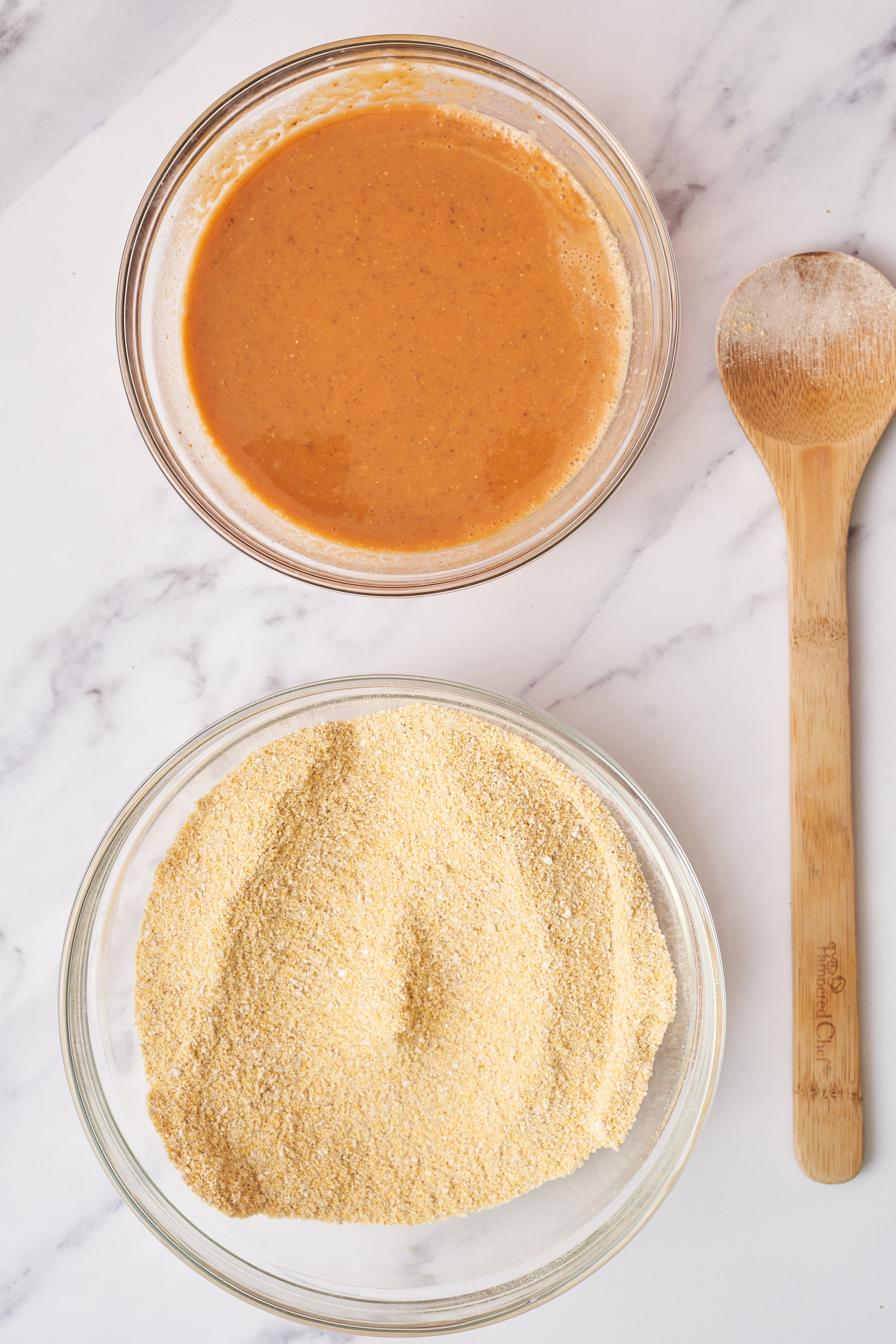 a bowl of mixed wet ingredients next to a bowl of cornmeal and a wooden spoon