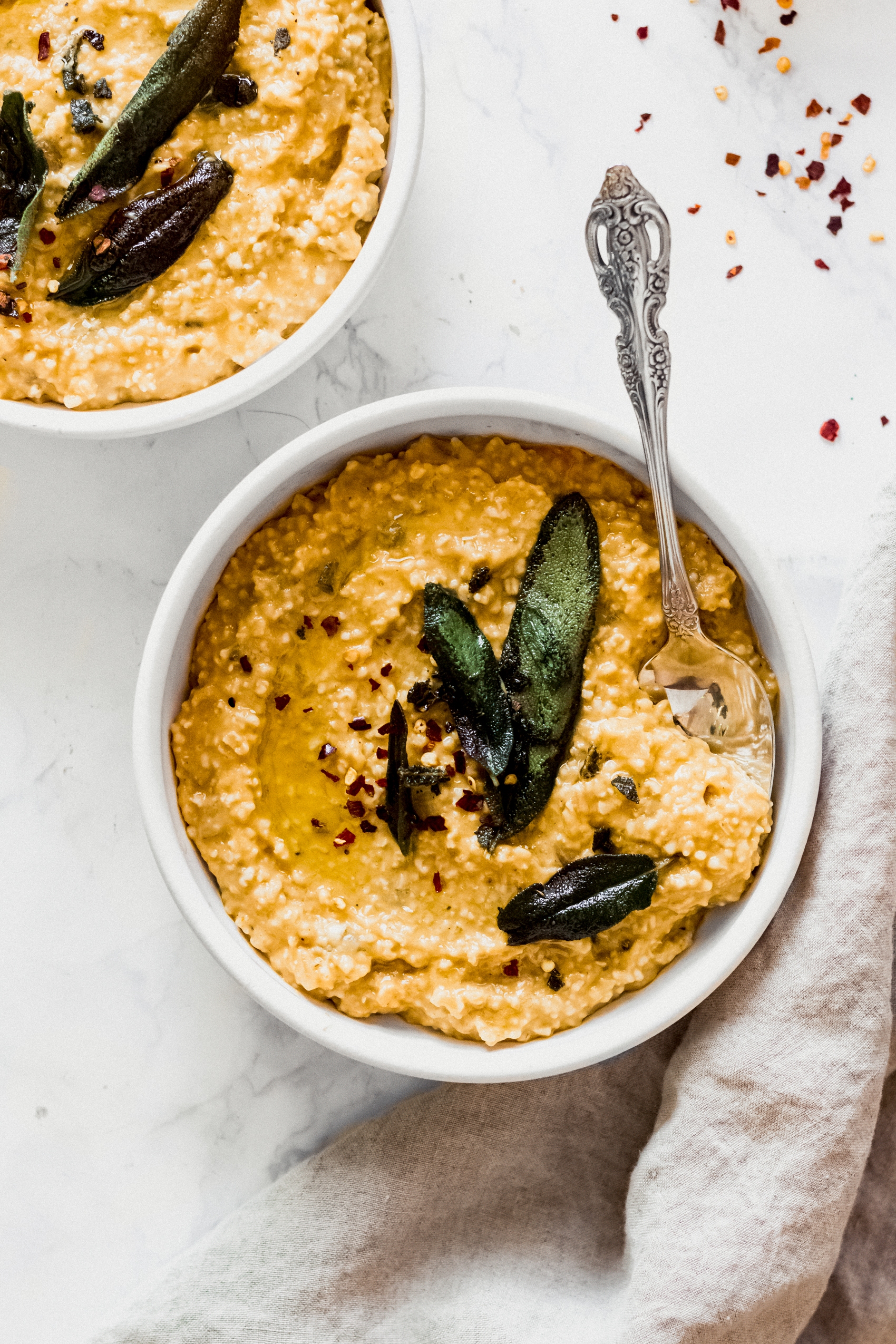 a spoon scooping into a bowl of savory pumpkin oats served with fried sage leaves