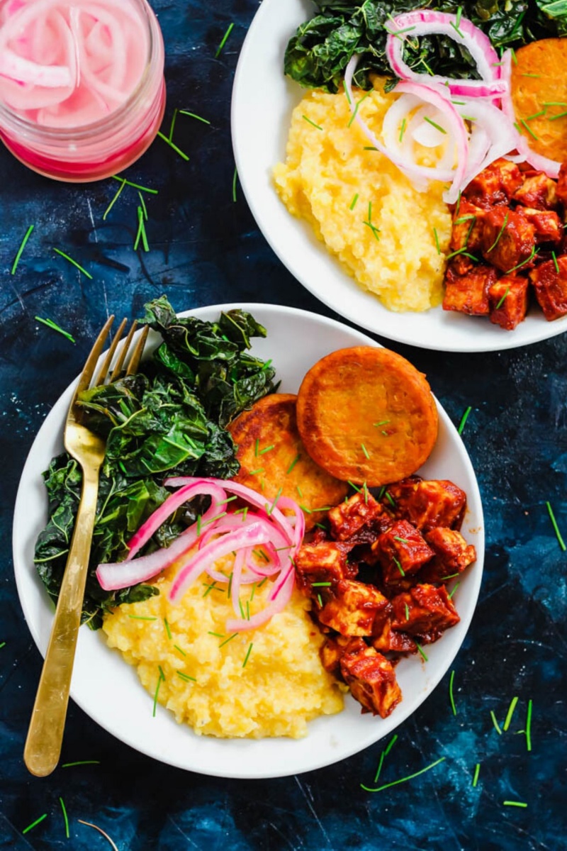 white plates of yellow grits with a gold fork and pink pickled onions