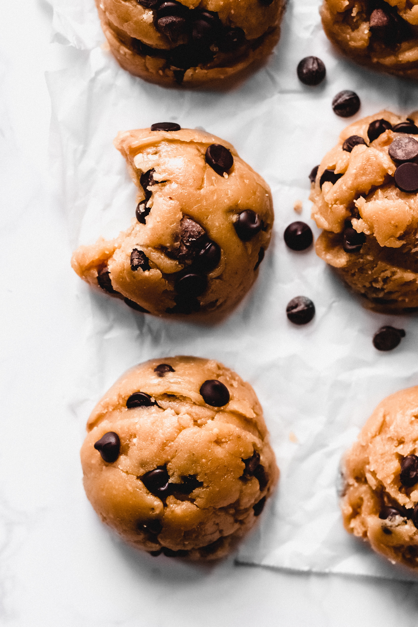 a closeup of four edible chocolate chip cookie dough balls, one with a bite missing