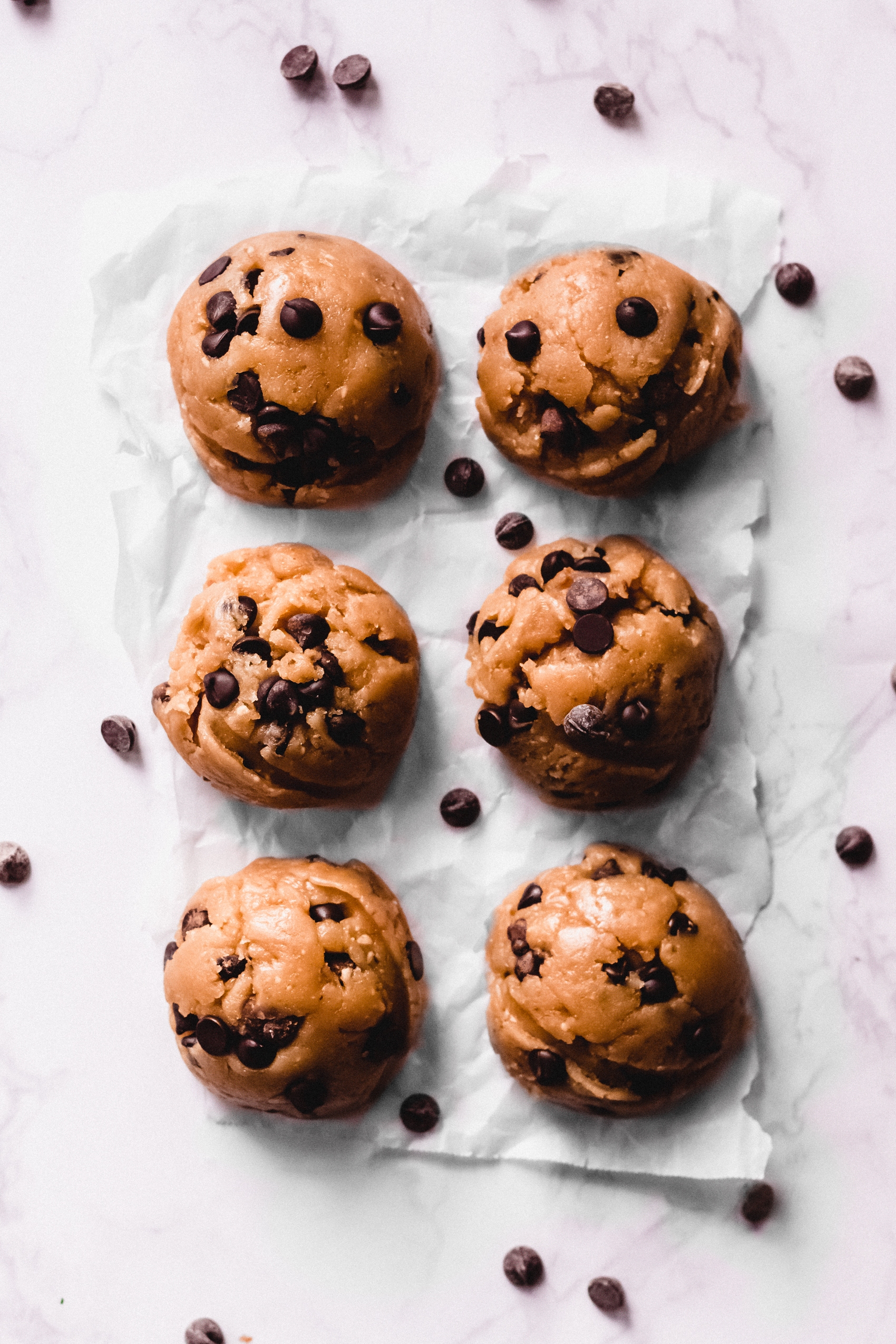 six chocolate chip cookie dough balls surrounded by scattered chocolate chips