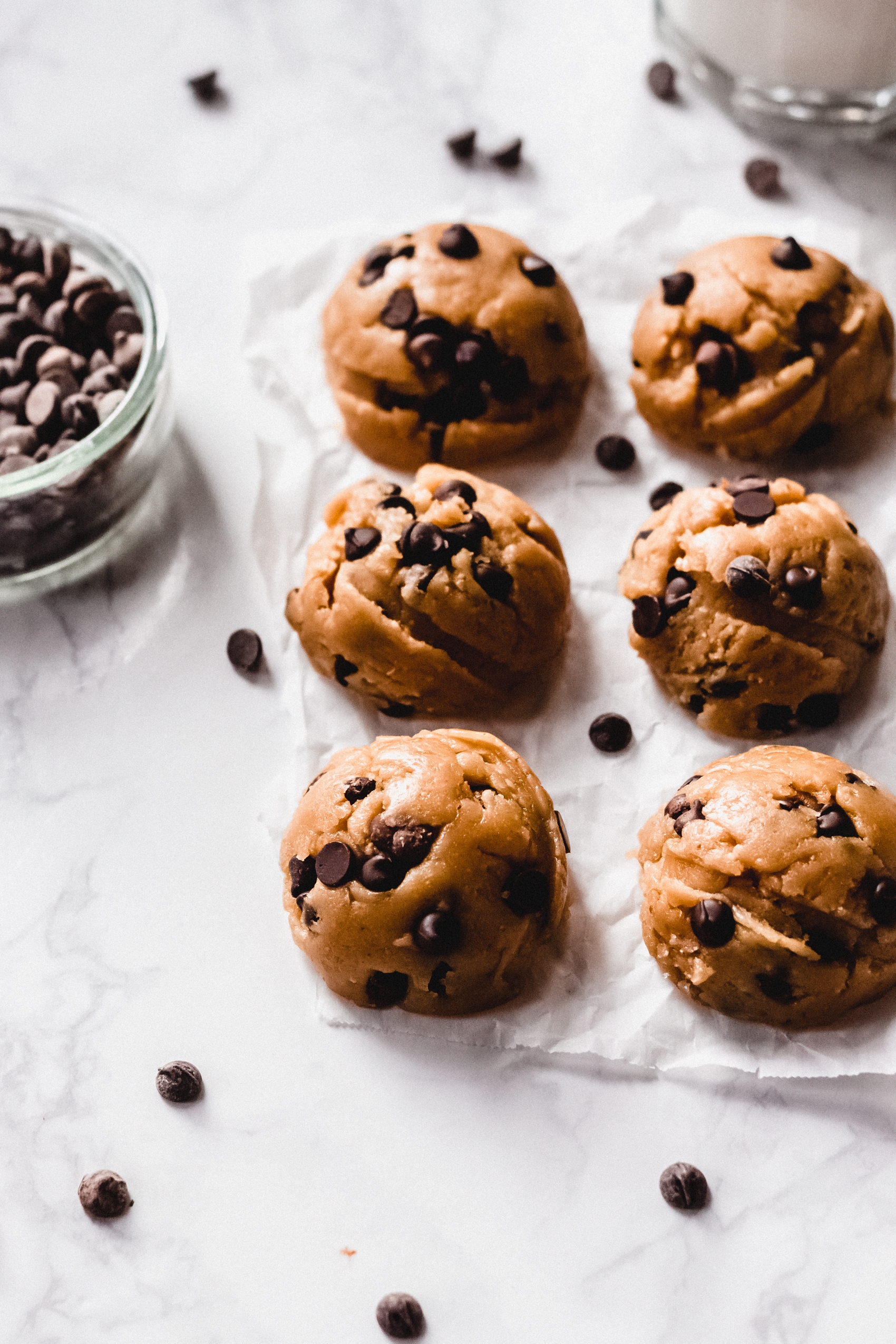 six chocolate chip cookie dough balls next to a bowl of chocolate chips