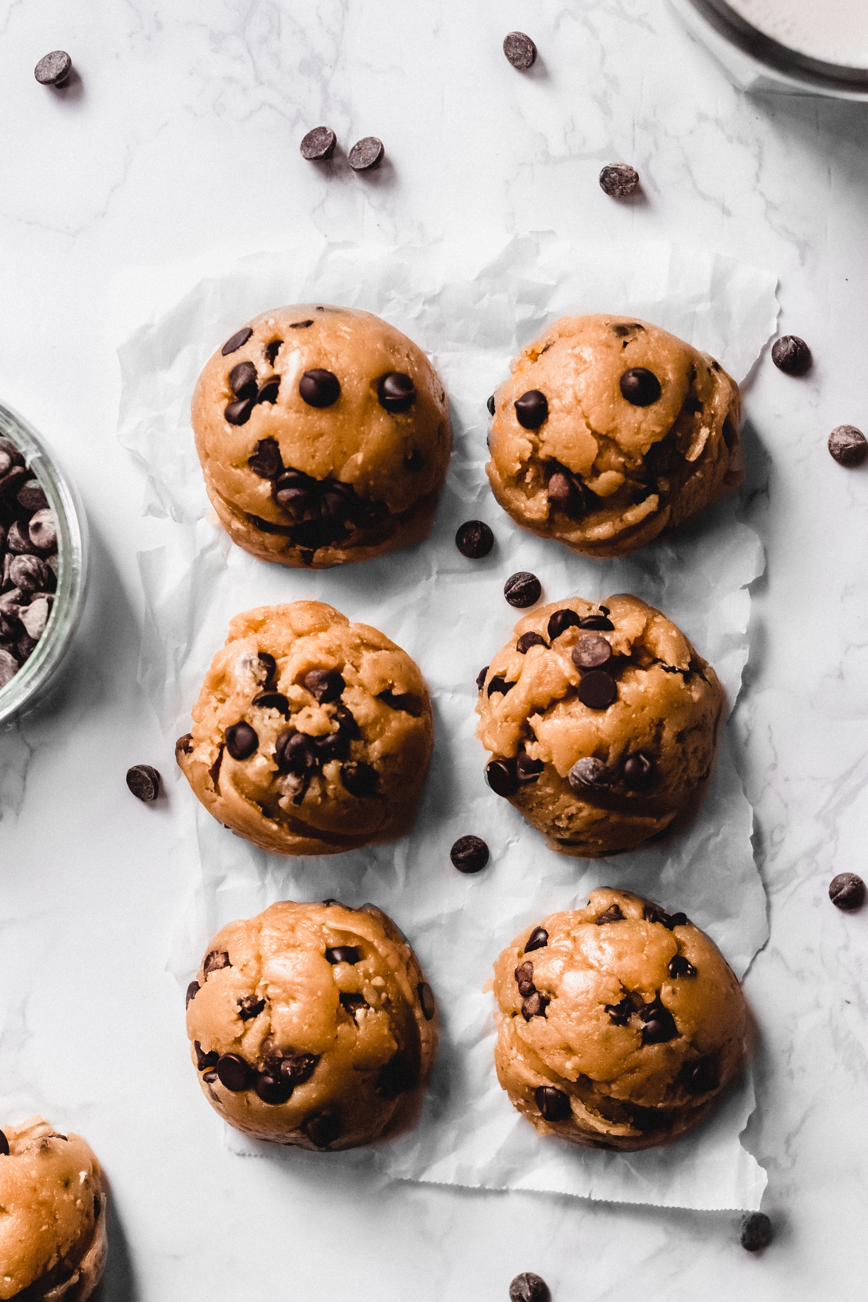 six chocolate chip cookie dough balls next to a bowl of chocolate chips